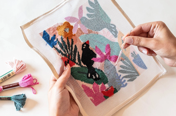 Close-up of hands stitching a colorful needlepoint canvas using tapestry needle and thread