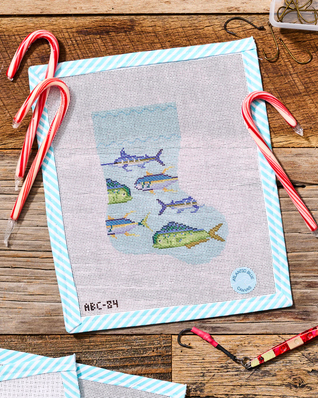 Painted needlepoint canvas with fish design, candy canes, and craft tools for a handmade Christmas stocking project