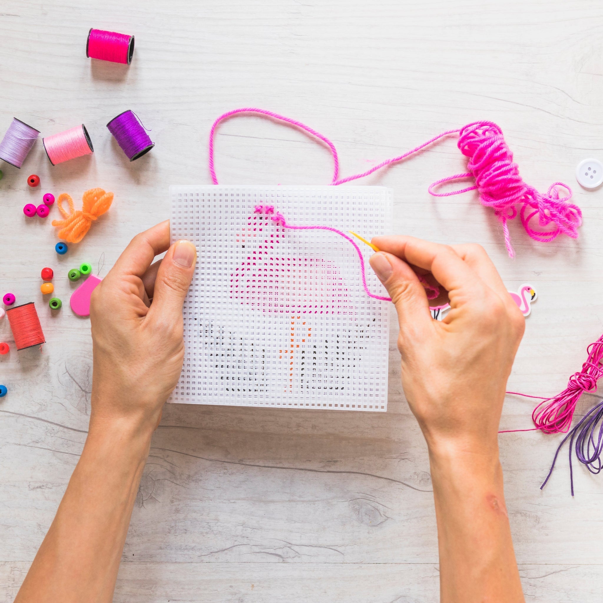 Hands creating stitch art on mesh canvas with colorful threads, ideal for beginners learning how to needlepoint with accessories.