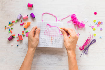 Hands creating stitch art on mesh canvas with colorful threads, ideal for beginners learning how to needlepoint with accessories.