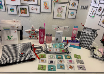 Table with needlepoint designs, accessories, and stitched items, showing the variety offered by modern needlepoint shops online.