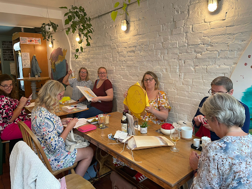 Needlepoint community gathering for slow living crafts and mindful stitching, sharing creative healing stories and mental health benefits.
