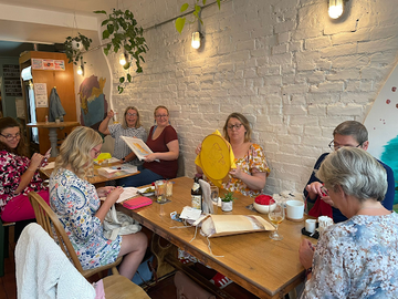 Needlepoint community gathering for slow living crafts and mindful stitching, sharing creative healing stories and mental health benefits.