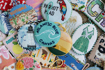 Atlantic Blue needlepoint ornaments displayed together, featuring round holiday designs and a central logo canvas for home décor.