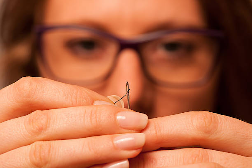 Woman learning how to thread a needle for needlepoint using a tapestry needle and proper threading technique