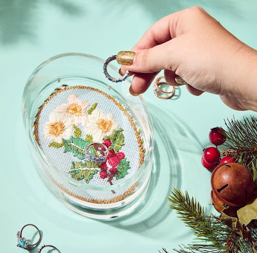 Woman placing rings into an oval glass bowl with a floral decorative needlepoint design, a stylish finished needlepoint home decor idea.