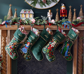 Personalized needlepoint stockings hanging from a fireplace mantel with Christmas decor, ideal holiday needlepoint projects