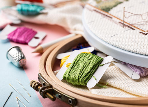 Needlepoint canvas, threads, frame, and accessories arranged together, showing how to needlepoint with a complete beginner kit.